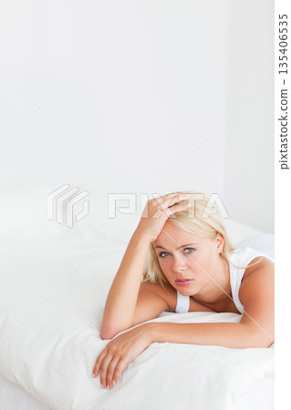 Woman in her twenties lying on white duvet in bedroom wearing tank top, copy space Woman in her twenties lying on white duvet in bedroom wearing tank top, copy space 135406535