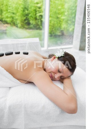 Female receiving hot stone massage on massage table in spa with flower in hair, copy space 135406546