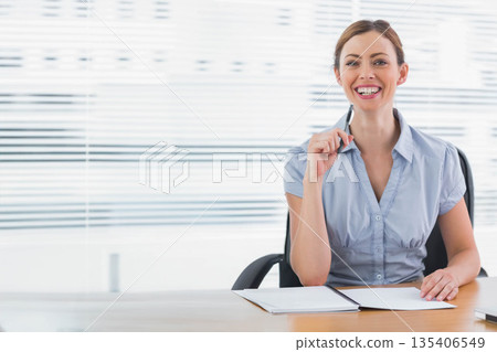 Woman wearing blue shirt sitting at desk in office writing in notebook with pen, copy space 135406549