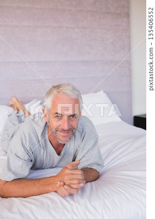 Senior man lying in bedroom on bed with white linens and headboard smiling toward camera Senior man lying in bedroom on bed with white linens and headboard smiling toward camera 135406552