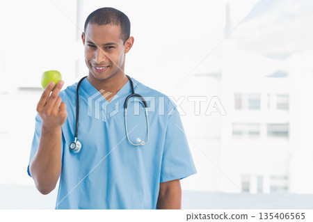African American male doctor in scrubs with stethoscope holding green apple at clinic, copy space African American male doctor in scrubs with stethoscope holding green apple at clinic, copy space 135406565