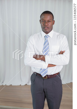 African American man standing with crossed arms in studio with light curtains wearing striped tie 135406577