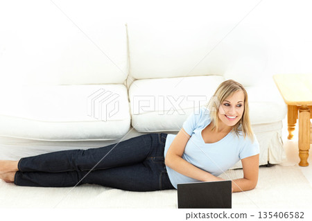 Woman reclining on carpet in living room using laptop beside white sofa and side table Woman reclining on carpet in living room using laptop beside white sofa and side table 135406582