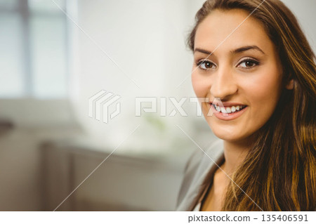 Woman in blazer smiling while sitting at office desk with potted plant and window, copy space Woman in blazer smiling while sitting at office desk with potted plant and window, copy space 135406591