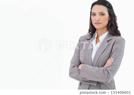 Businesswoman standing with crossed arms in studio wearing grey blazer, white shirt, copy space 135406601