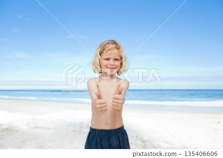 School-aged boy standing barefoot on seaside sand wearing dark blue swim shorts holding thumbs up School-aged boy standing barefoot on seaside sand wearing dark blue swim shorts holding thumbs up 135406606