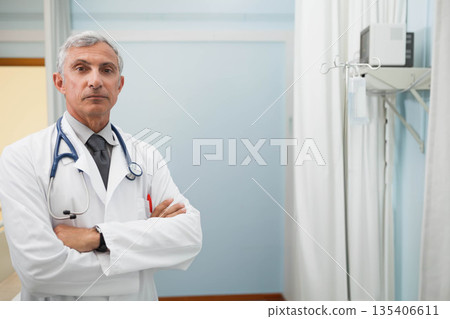 Middle-aged male doctor standing in hospital room near IV pole, monitor, stethoscope, copy space 135406611