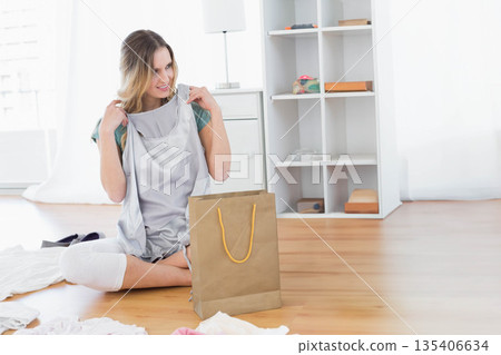 Woman sitting on floor at home holding gray sleeveless dress from brown paper bag, copy space Woman sitting on floor at home holding gray sleeveless dress from brown paper bag, copy space 135406634