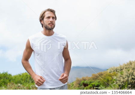 Man jogging through rural hillside trail in sleeveless shirt and shorts among shrubs 135406664