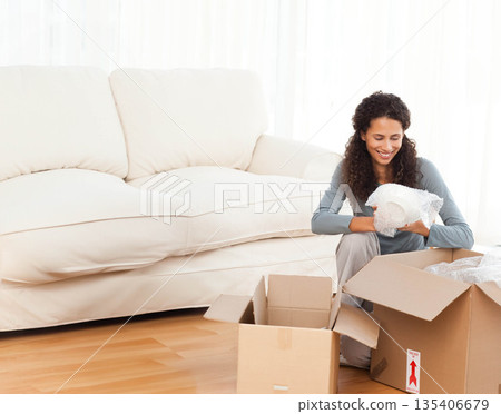Woman unpacking bubble-wrapped ceramic dish on wood floor at home amid cardboard boxes, copy space 135406679
