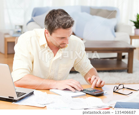 Man calculating finances using calculator and laptop on low wooden table in living room 135406687