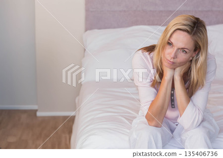 Woman in her thirties sitting on bed leaning forward with chin resting in hands, copy space Woman in her thirties sitting on bed leaning forward with chin resting in hands, copy space 135406736