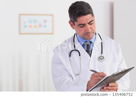 Senior male physician wearing coat with stethoscope writing on clipboard in exam room, copy space Senior male physician wearing coat with stethoscope writing on clipboard in exam room, copy space 135406752