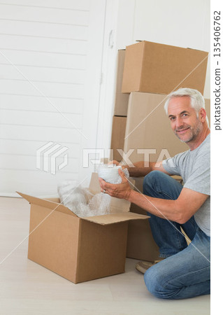 Senior man kneeling at home packing items into cardboard moving box with bubble wrap, copy space 135406762