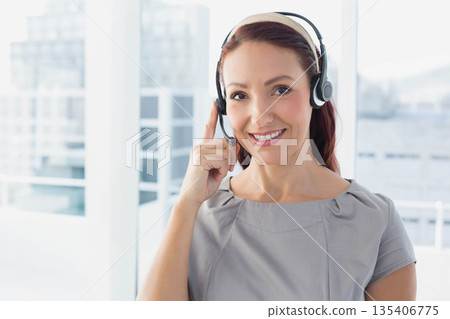 Woman adjusting headset with finger in high-rise office overlooking city skyline, copy space Woman adjusting headset with finger in high-rise office overlooking city skyline, copy space 135406775