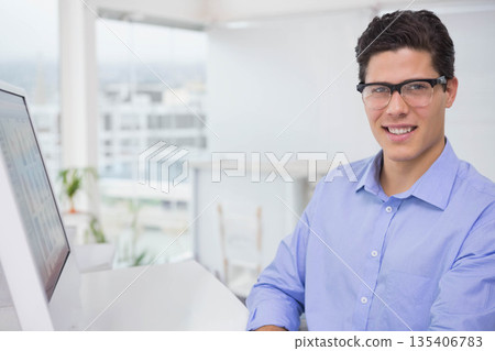 Male professional sitting at desk in office viewing charts on monitor, potted plants, copy space 135406783
