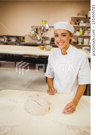Female chef smiling behind worktable in bakery kitchen, kneading dough in chef uniform, copy space 135406785