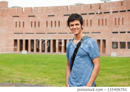 Male student smiling on lawn at campus carrying dark shoulder bag in front of brick columns 135406791
