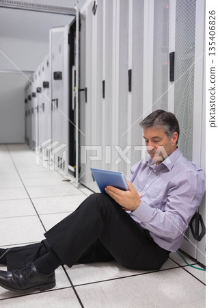 IT professional man sitting on data center floor tiles inspecting equipment with tablet, copy space 135406826