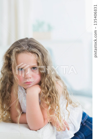 Girl sitting on sofa with throw cushion in living room, resting chin on hand near plant 135406831