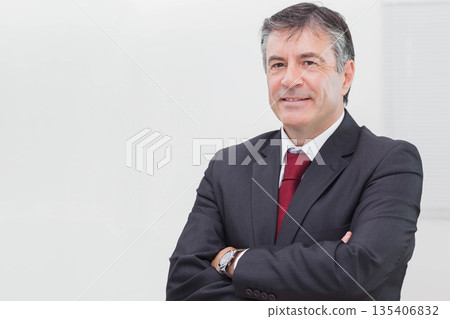 Middle-aged male executive crossing arms in office wearing suit red tie with wristwatch, copy space Middle-aged male executive crossing arms in office wearing suit red tie with wristwatch, copy space 135406832