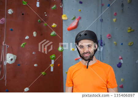 Male climber gripping holds and ropes while climbing wall at gym in orange shirt and helmet Male climber gripping holds and ropes while climbing wall at gym in orange shirt and helmet 135406897