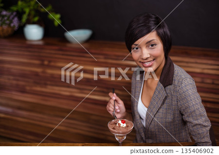 Adult Asian woman in blazer tasting chocolate mousse at wooden counter by potted plant, copy space Adult Asian woman in blazer tasting chocolate mousse at wooden counter by potted plant, copy space 135406902