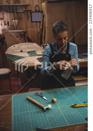 Senior woman wearing apron stitching leather by hand at workshop bench with cutting mat, copy space Senior woman wearing apron stitching leather by hand at workshop bench with cutting mat, copy space 135406917
