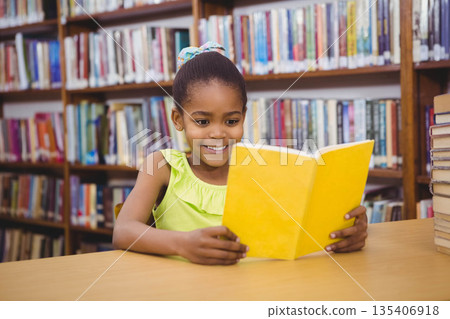African American girl sitting at wooden table reading yellow book with stacked books in library African American girl sitting at wooden table reading yellow book with stacked books in library 135406918