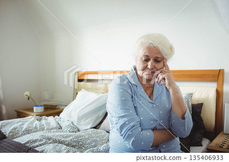 Senior woman sitting on bed edge in bedroom with patterned duvet wearing heart print pajamas 135406933