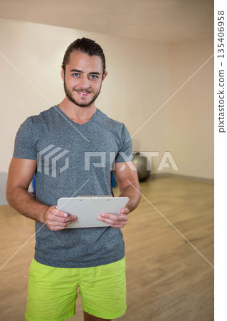 Male instructor holding clipboard while guiding workout in fitness studio with exercise ball Male instructor holding clipboard while guiding workout in fitness studio with exercise ball 135406958