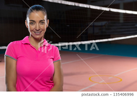 Athletic woman wearing pink polo shirt standing on court before net and yellow circle, copy space 135406996