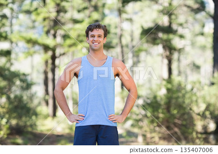 Man running on forest trail in blue sleeveless shirt and navy shorts under sunlit pine canopy 135407006