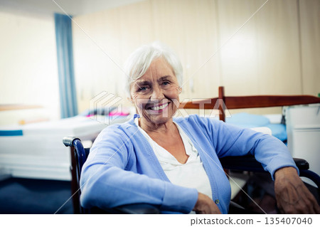 Senior woman sitting in wheelchair in care room beside bed with railings and blue curtain Senior woman sitting in wheelchair in care room beside bed with railings and blue curtain 135407040