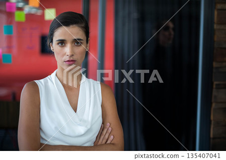 Woman standing in office room surveying sticky notes on red accent wall through glass partition 135407041