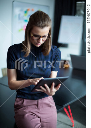 Woman holding tablet at dark table in office with whiteboard sticky notes, flip chart and laptop Woman holding tablet at dark table in office with whiteboard sticky notes, flip chart and laptop 135407042