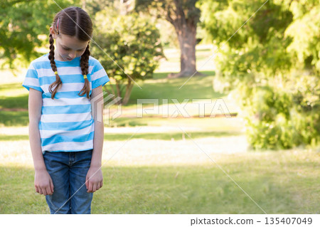 Girl standing on sunlit grassy lawn in park with braided pigtails looking down, copy space Girl standing on sunlit grassy lawn in park with braided pigtails looking down, copy space 135407049