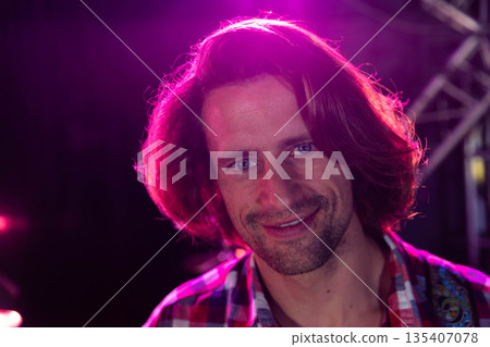 Mid-thirties man smiling and standing on stage under pink spotlights with metal lighting truss Mid-thirties man smiling and standing on stage under pink spotlights with metal lighting truss 135407078