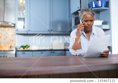Senior African American woman holding smartphone, reading document at kitchen island, copy space Senior African American woman holding smartphone, reading document at kitchen island, copy space 135407115