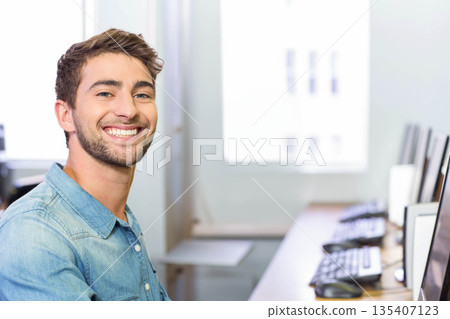 Man wearing denim shirt sitting at desk in office typing on keyboard near monitors, copy space 135407123