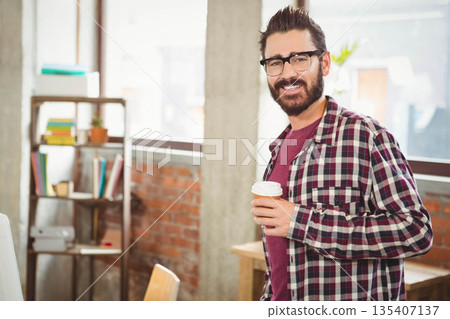Man holding takeaway coffee cup and smiling in loft office by bookshelf, copy space 135407137