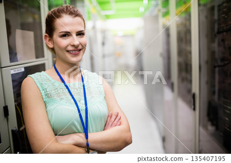 Female IT technician crossing arms wearing ID badge in server room by server racks, copy space Female IT technician crossing arms wearing ID badge in server room by server racks, copy space 135407195