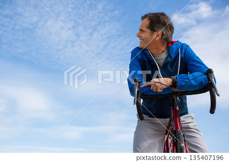 Male cyclist leaning on red bike bars wearing jacket with smartwatch on cycling path, copy space 135407196