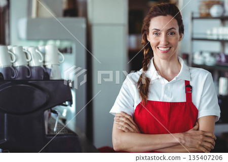 Female barista wearing red apron and smiling at counter with espresso machine, copy space Female barista wearing red apron and smiling at counter with espresso machine, copy space 135407206