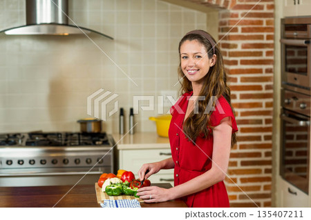 Adult woman wearing red dress slicing vegetables using chef's knife in home kitchen, copy space 135407211