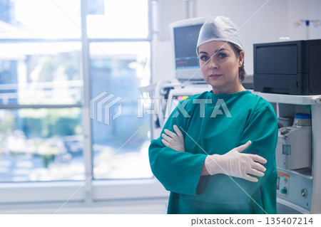 Senior woman surgeon wearing scrubs standing near anesthesia machine in surgical suite, copy space 135407214