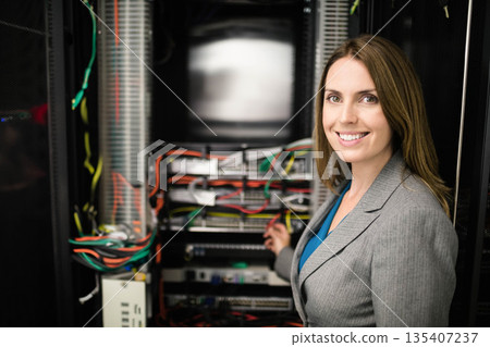 Mid adult female network engineer wearing blazer managing cables at rack in server room, copy space Mid adult female network engineer wearing blazer managing cables at rack in server room, copy space 135407237