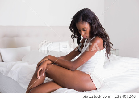 African American woman wearing sleepwear sitting on bed with pillows, looking down copy space 135407246