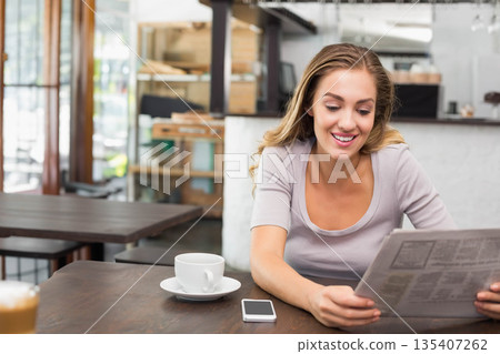 Woman reading newspaper at wooden cafe table holding coffee cup and smartphone, copy space 135407262