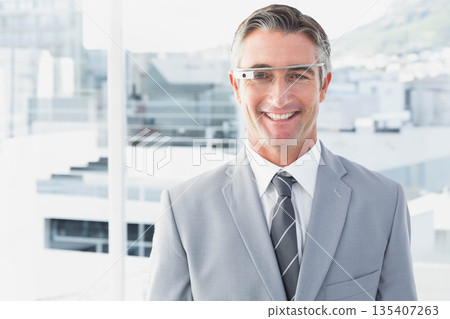 Businessman smiling in front of floor-to-ceiling window wearing suit and smart glasses, copy space Businessman smiling in front of floor-to-ceiling window wearing suit and smart glasses, copy space 135407263